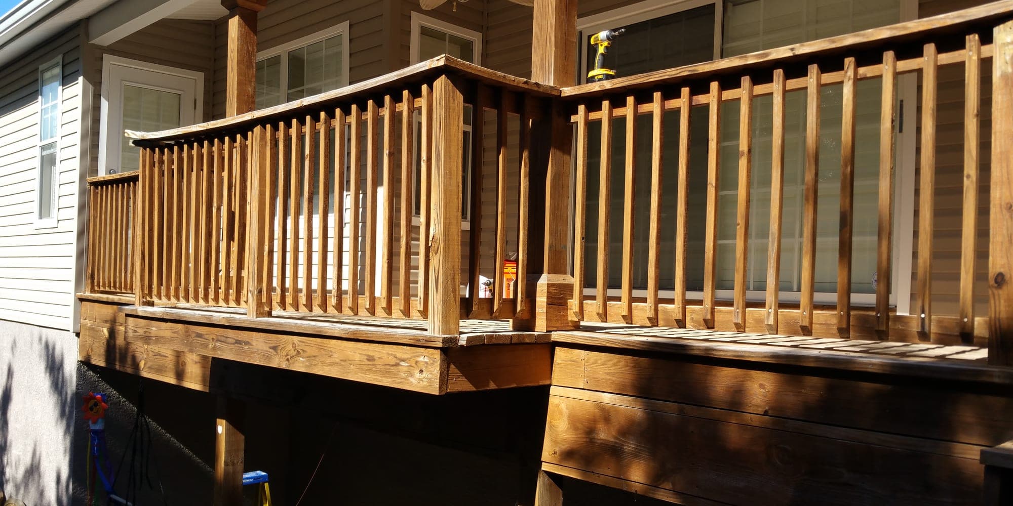 Stained wood deck with custom milled railing attached to the back of a home