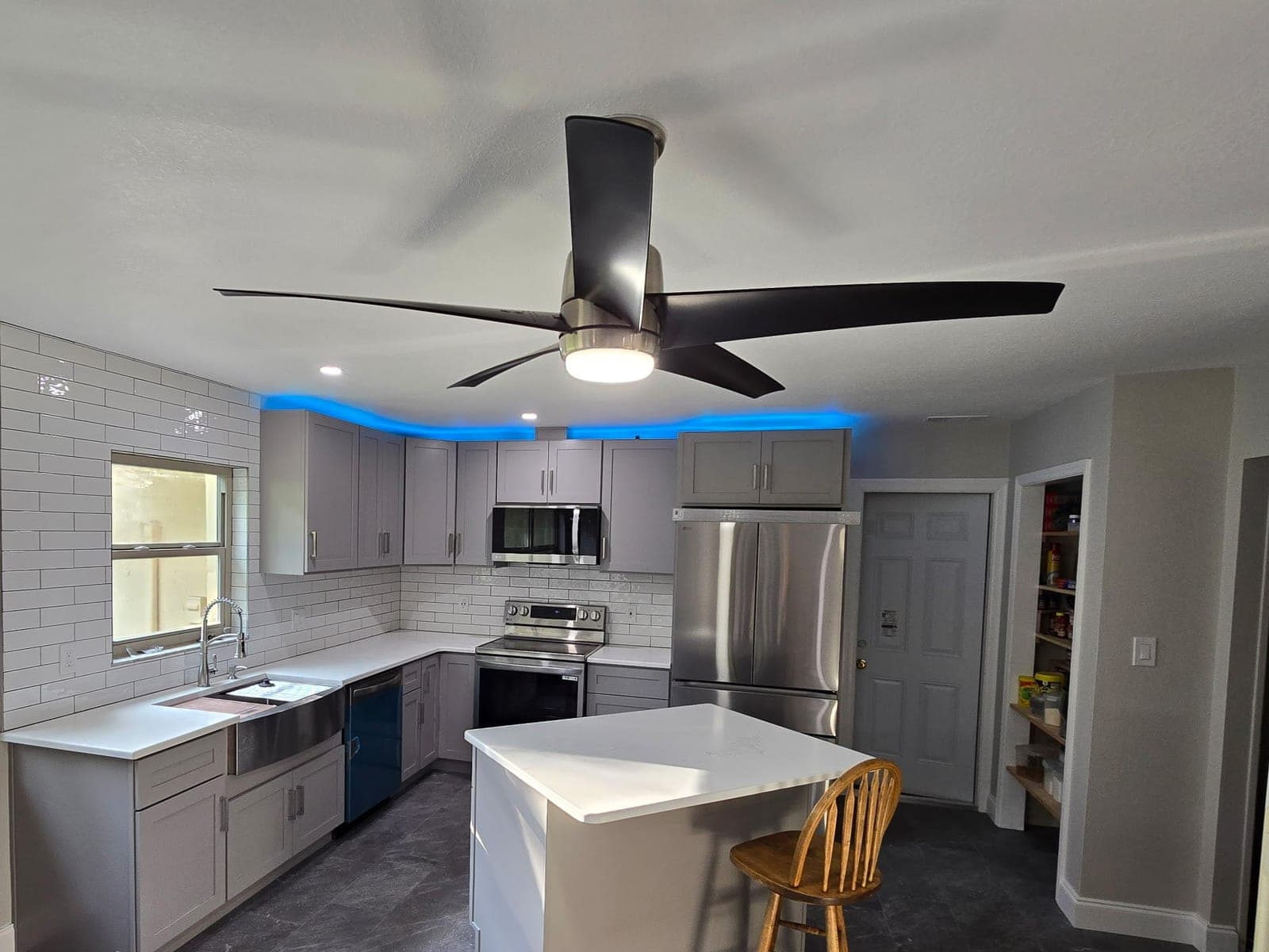 Same kitchen after renovation with gray shaker cabinets, quartz island, subway tile backsplash, and stainless appliances