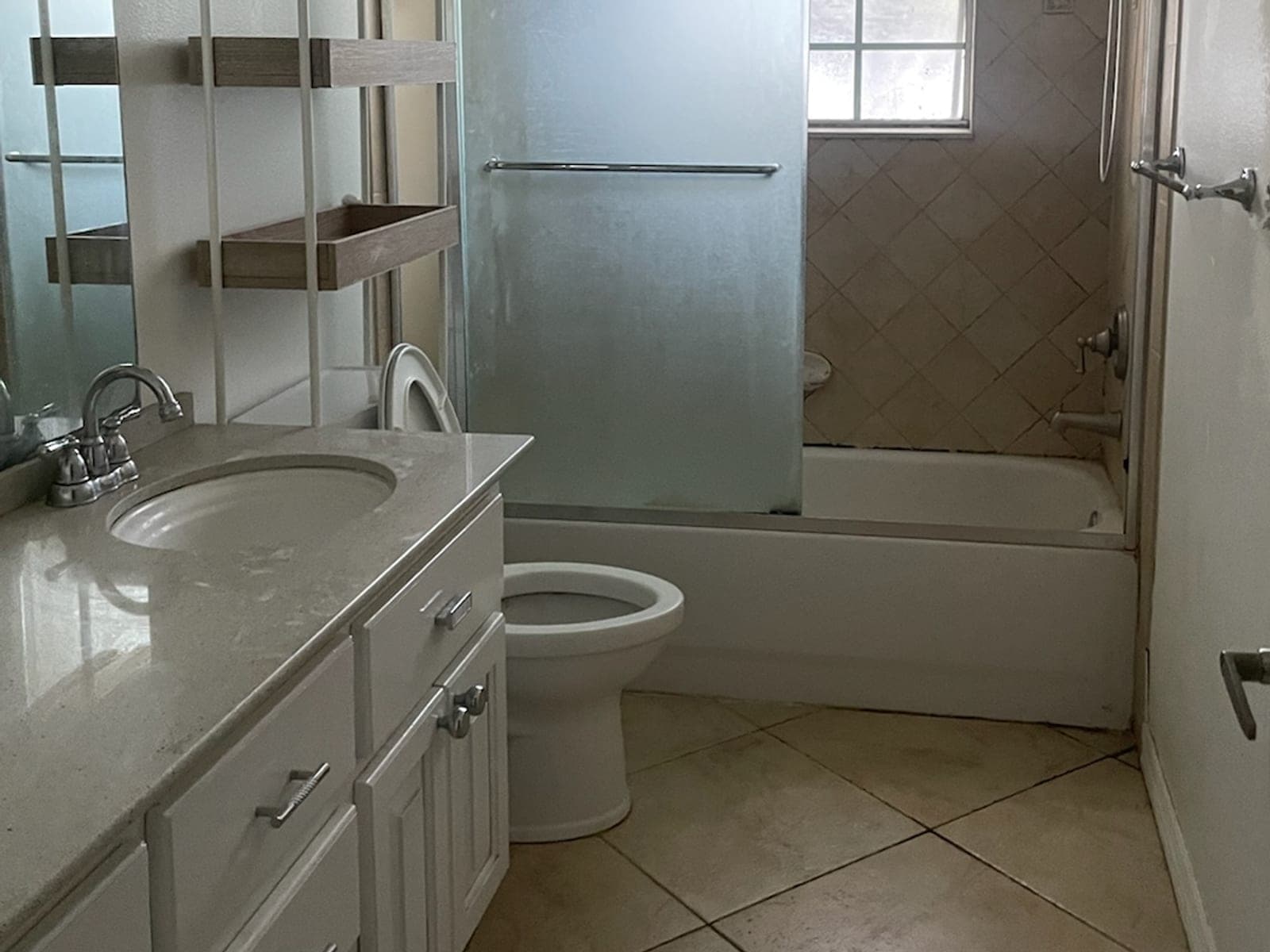 Bathroom before remodel with beige diamond tile tub surround, frosted sliding glass doors, and a dated vanity