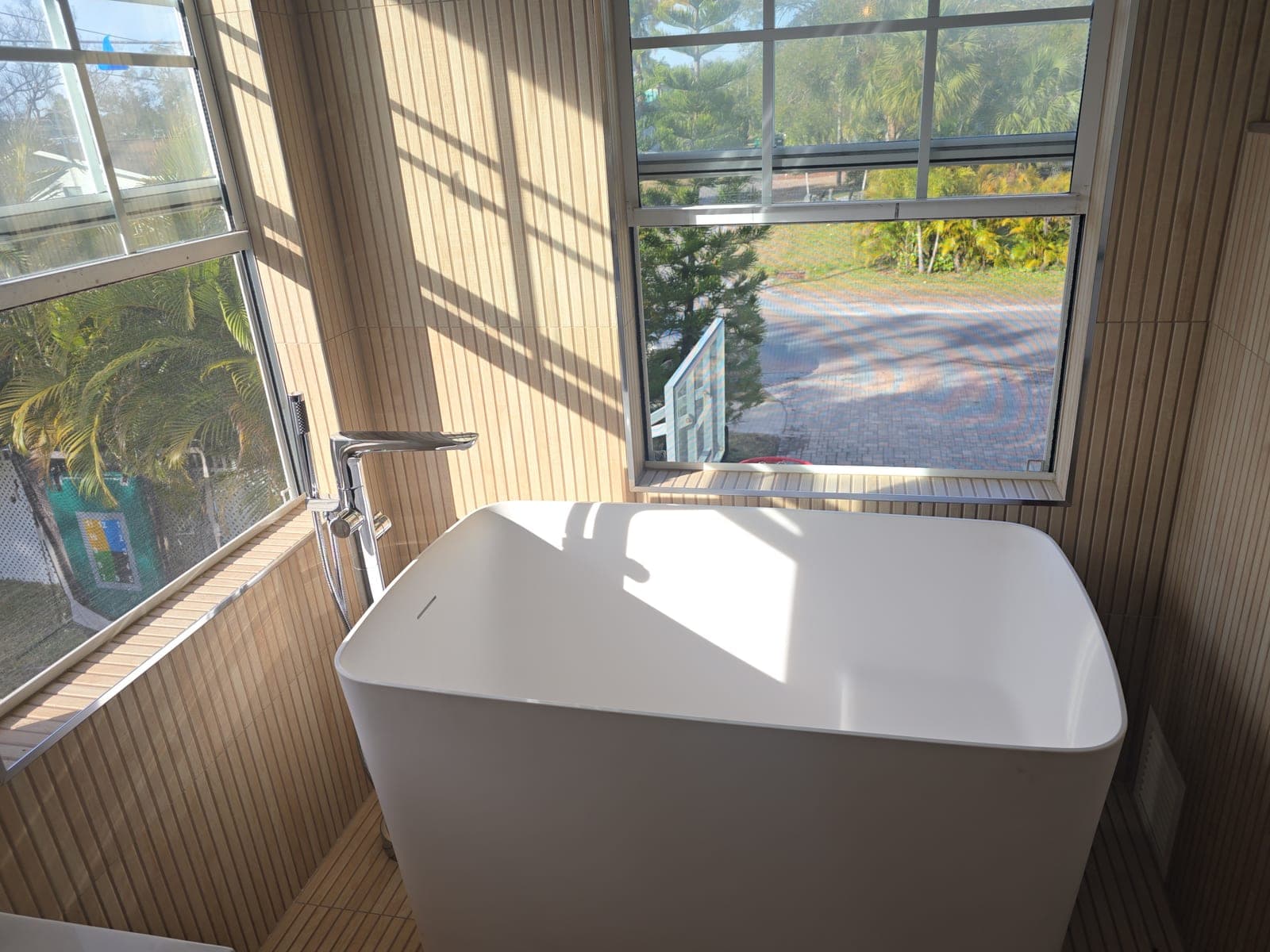 Freestanding soaking tub set in a window nook with fluted tile surround