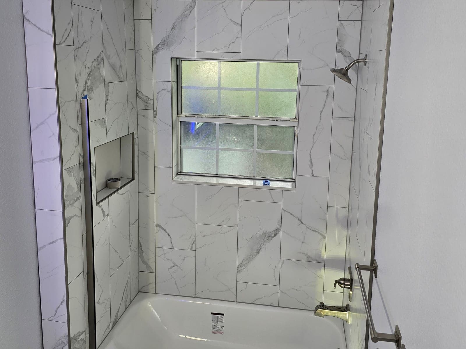Marble look tile tub surround with a recessed niche and glass door