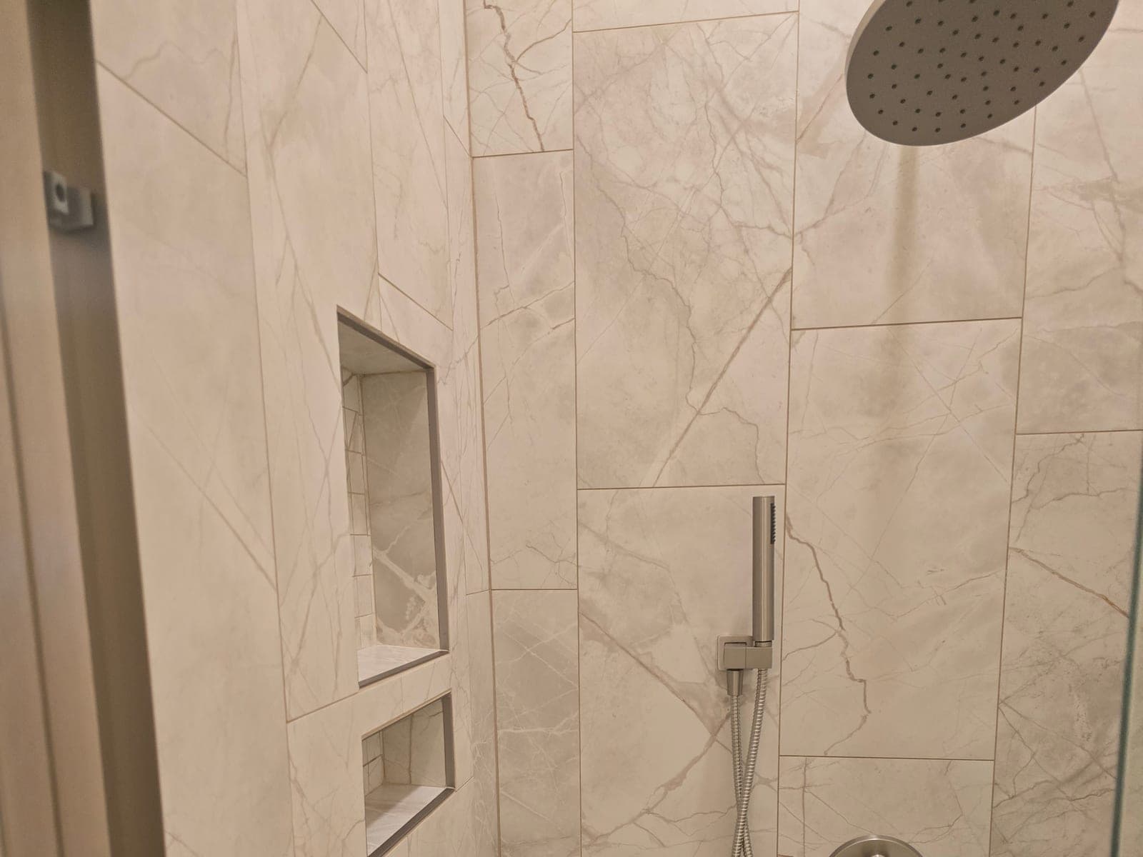 Walk in shower with marble look tile, stacked recessed niches, rainfall head, and handheld sprayer