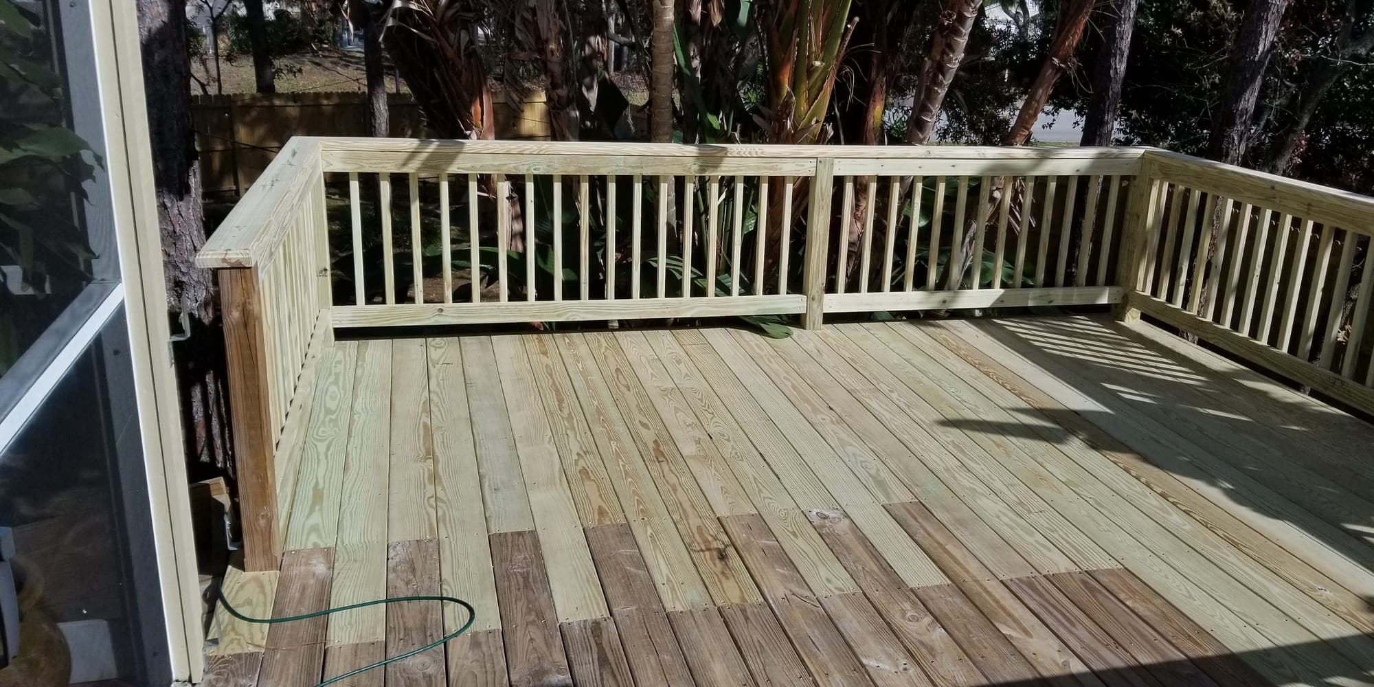 Completed pressure treated deck with railings surrounded by mature landscaping