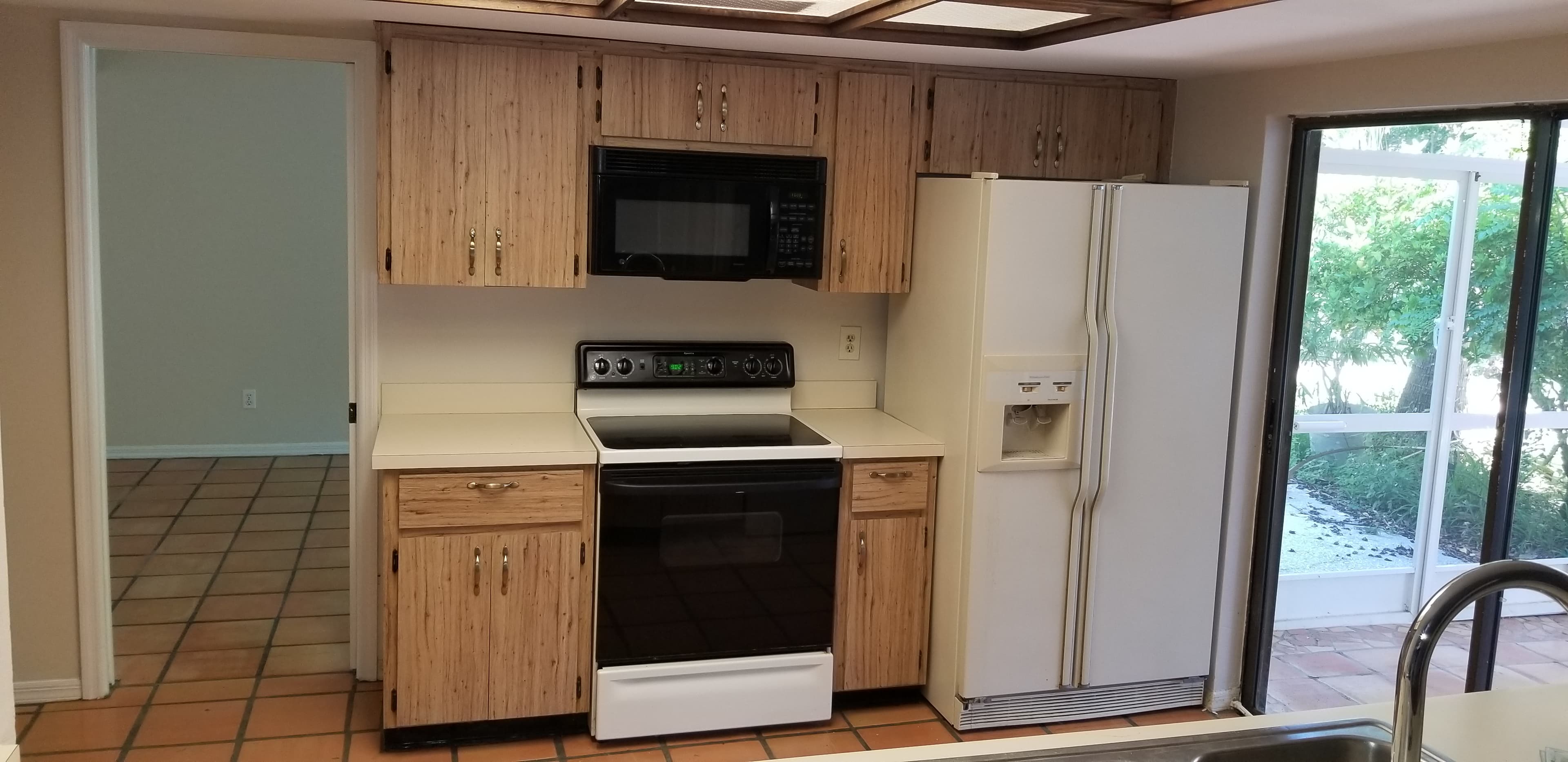 Kitchen before remodel with dated wood grain laminate cabinets and fluorescent ceiling box