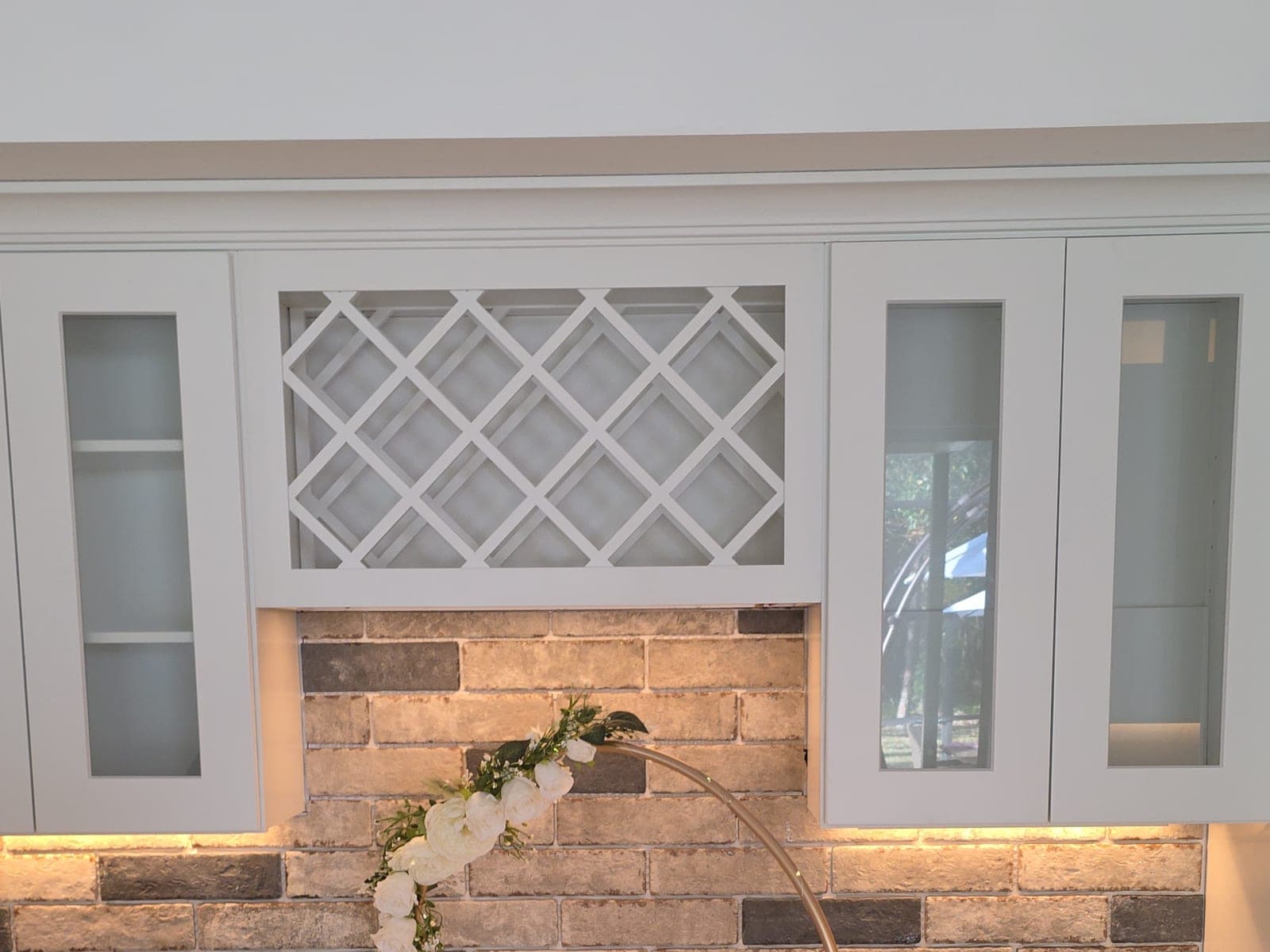 White kitchen cabinets with a built in lattice wine rack, glass front doors, and a brick backsplash lit from under the uppers