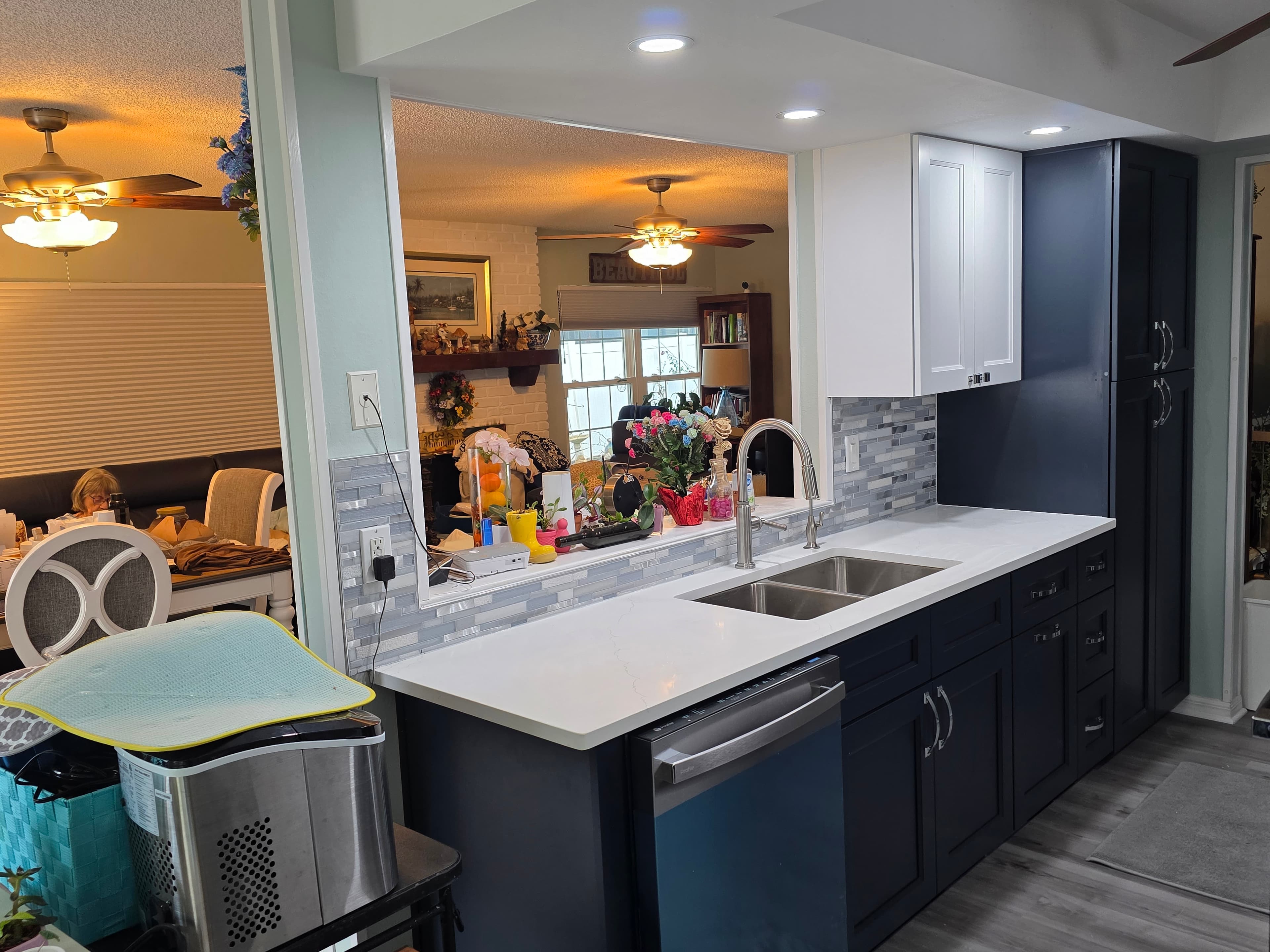 Galley kitchen renovation with navy base cabinets, white uppers, quartz counters, and glass mosaic backsplash